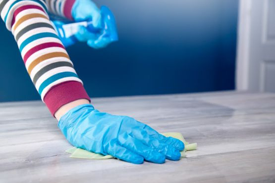 mano con guantes azules repasan mesa de oficina con paño